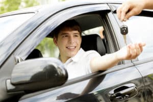 What Should Be My First Car? | Barney Brothers Off Road & Repair in Grand Junction, CO. Image of a new male driver inside a black car. He is smiling while accepting the new key of his car from a car salesman.