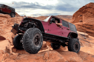 Suspension lift checkup, lift kits in Grand Junction, CO by Barney Brothers Off Road & Repairs. Image of a lifted Jeep Wrangler rock crawling on rugged red terrain with oversized tires and upgraded suspension, showcasing trail-ready performance and capability.